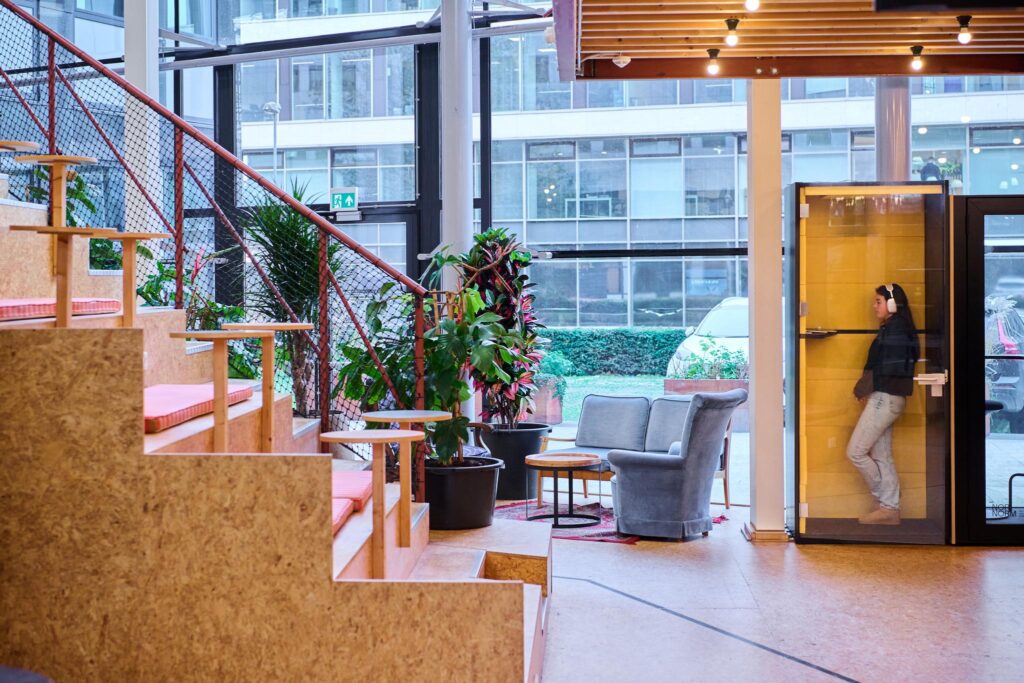 Moderne kantoorruimte aan het John M. Keynesplein met tribunezitplaatsen, planten, zithoek en een vrouw in een belcel.